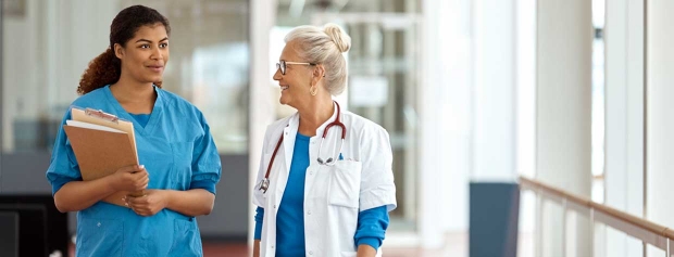 En sygeplejerske og en læge går på hospitalsgangen og taler sammen.